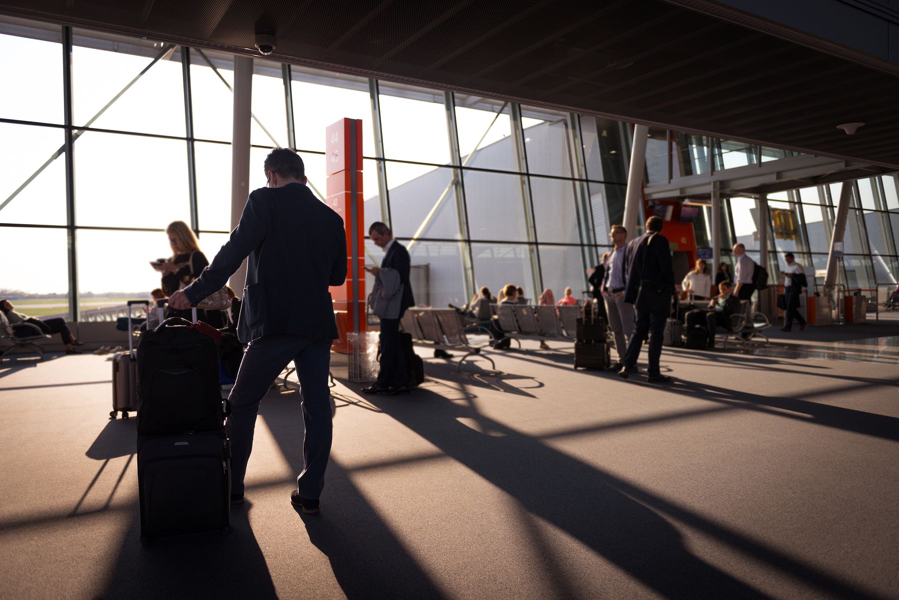 Travellers moving through a sunlit airport terminal